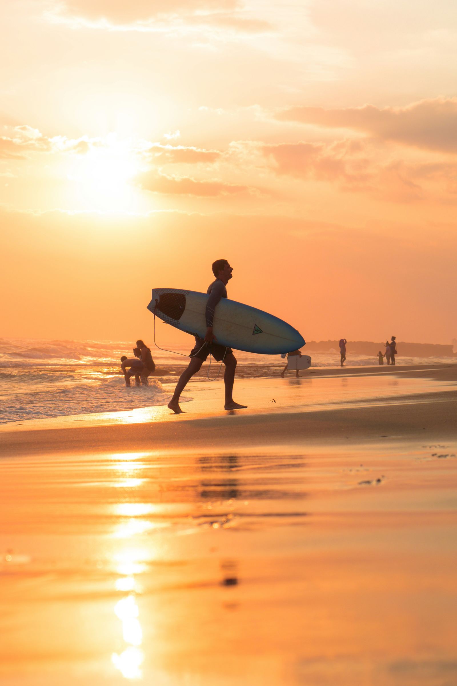 A surfer carrying a surfboard on Canggu Beach at sunset