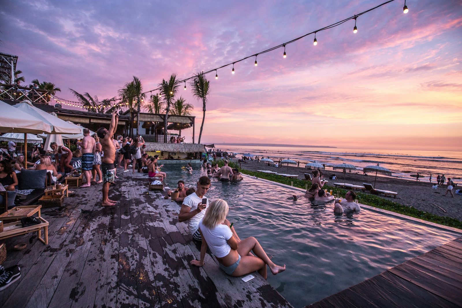 People relaxing at a beachfront pool club in Canggu at sunset